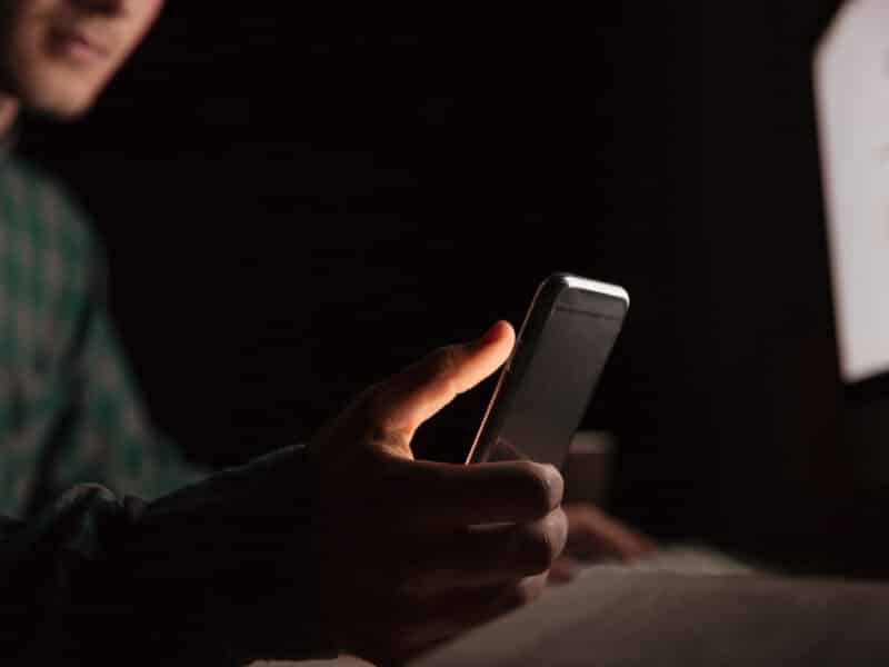 Man sitting at the table and using cell phone. The room is dark.