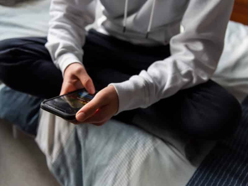 Close up of hands of teen boy in white sweater texting on phone.
