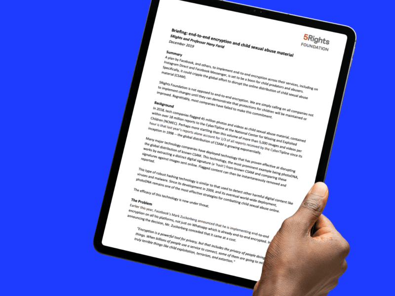 A hand is holding a tablet displaying a document titled "Briefing: End-to-End Encryption and Child Sexual Abuse Material" by 5Rights Foundation and Professor Hany Farid, dated December 2019. The text outlines concerns about the implementation of end-to-end encryption by major tech companies like Facebook and Instagram, and its potential to hinder efforts to combat child sexual abuse material (CSAM). The tablet is set against a bright blue background.