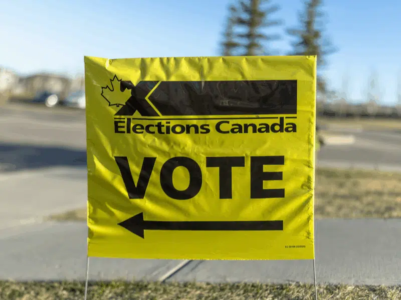 A vivid yellow sign from Elections Canada, displaying a maple leaf and bold black writing, signals a Canadian election voting site.