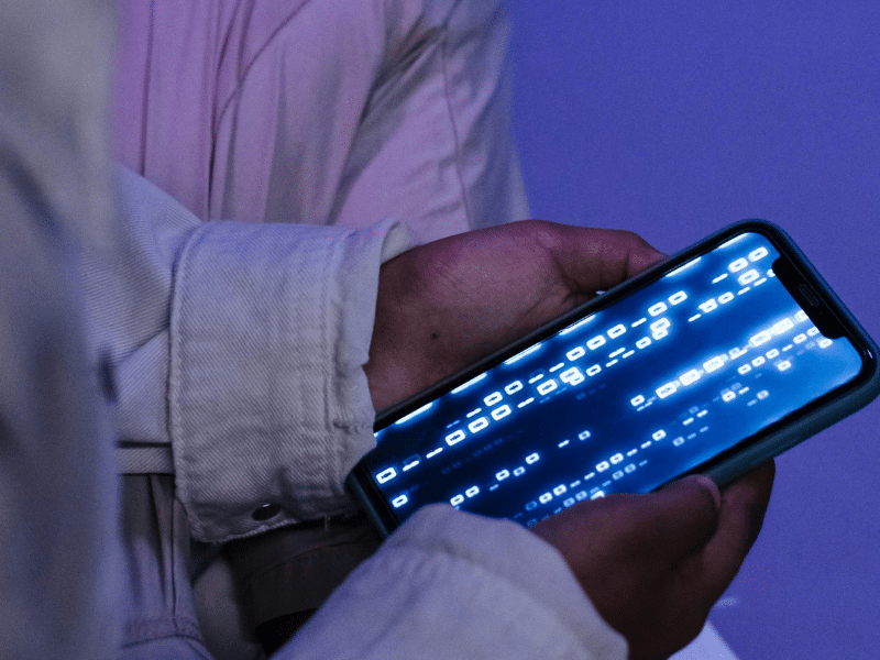 A young boy holding a cell phone displaying a bright blue screen, focused on the device in their hand.
