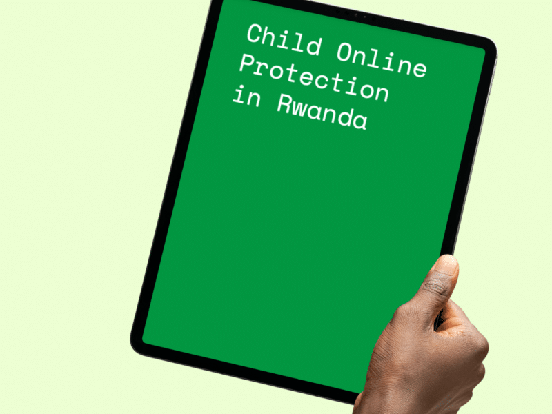 A hand holding a black tablet device with a bright green screen displaying the text "Child Online Protection in Rwanda" in white, typewriter-style font. The background of the image is a light green colour, providing contrast to the darker green of the tablet screen.
